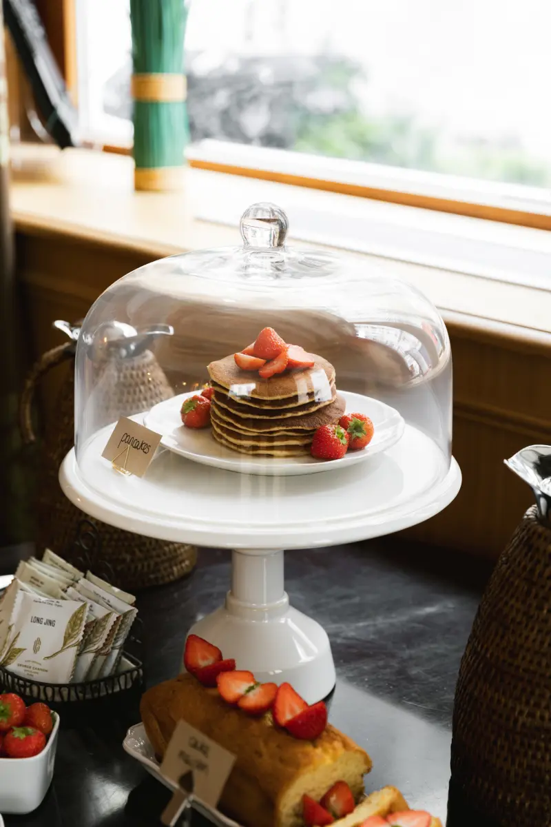 Cloche en verre avec tour de pancakes dores aux fraises sur presentoir blanc, sachets de the George Cannon