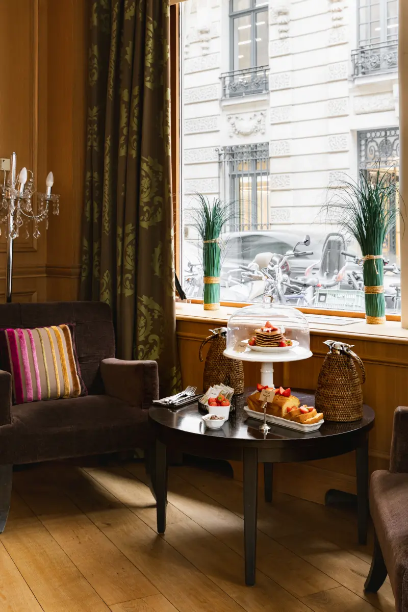 Salon de l'hotel Cordelia : fauteuil chocolat, table basse avec service tea time et vue sur facade haussmannienne