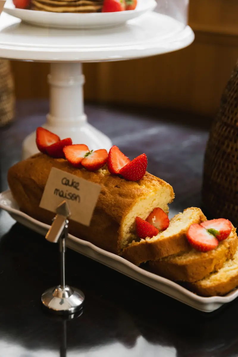 Gros plan sur cake maison tranche garni de fraises fraiches, etiquette Cake Maison sur support argente