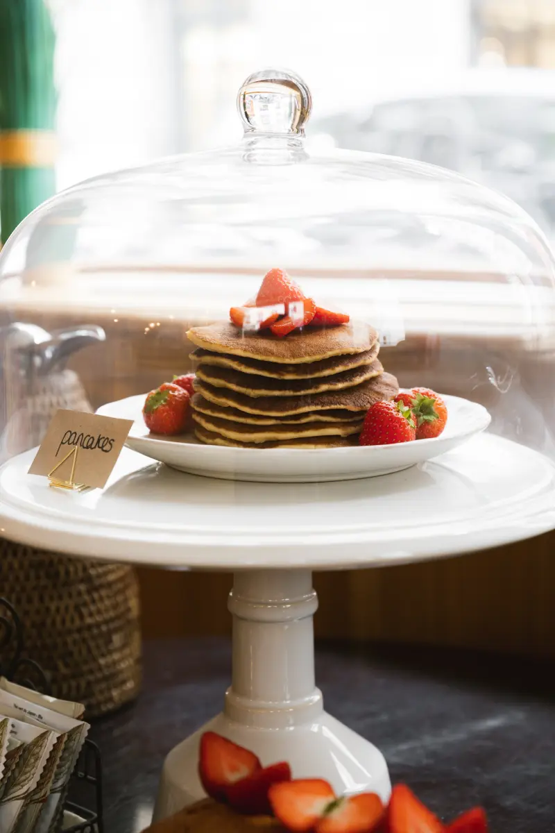 Presentoir blanc avec cloche en verre : pile de pancakes dores garnis de fraises fraiches, etiquette pancakes