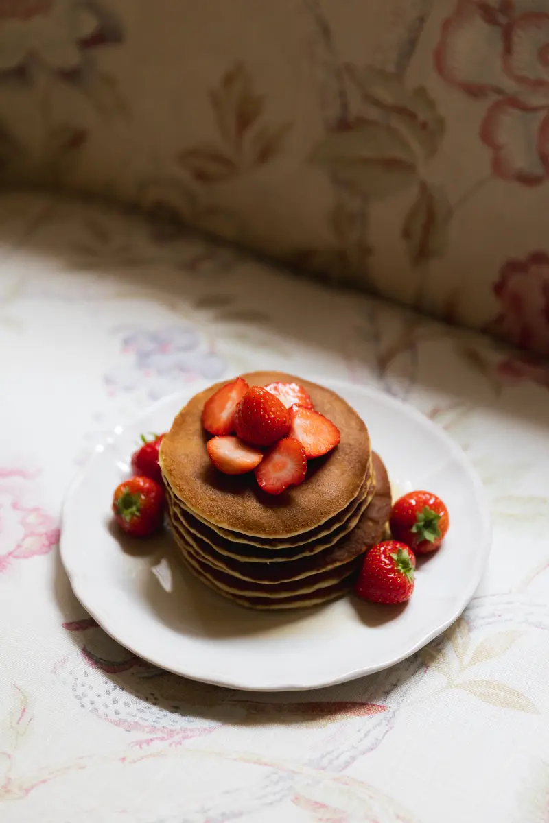 Assiette Hotel Cordelia avec pile de pancakes dores garnis de fraises fraiches, sur dessus-de-lit fleuri