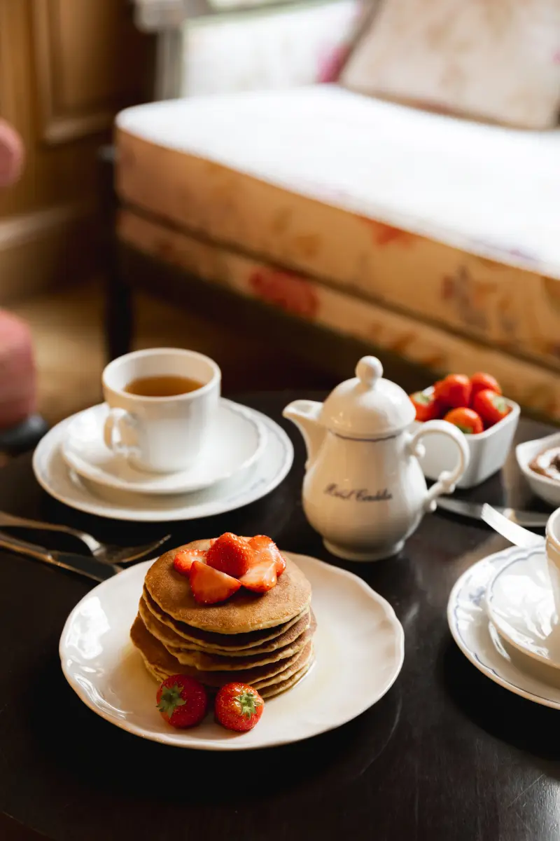 Table en chambre avec pancakes aux fraises, theiere et tasse Hotel Cordelia, bol de fraises et Nutella