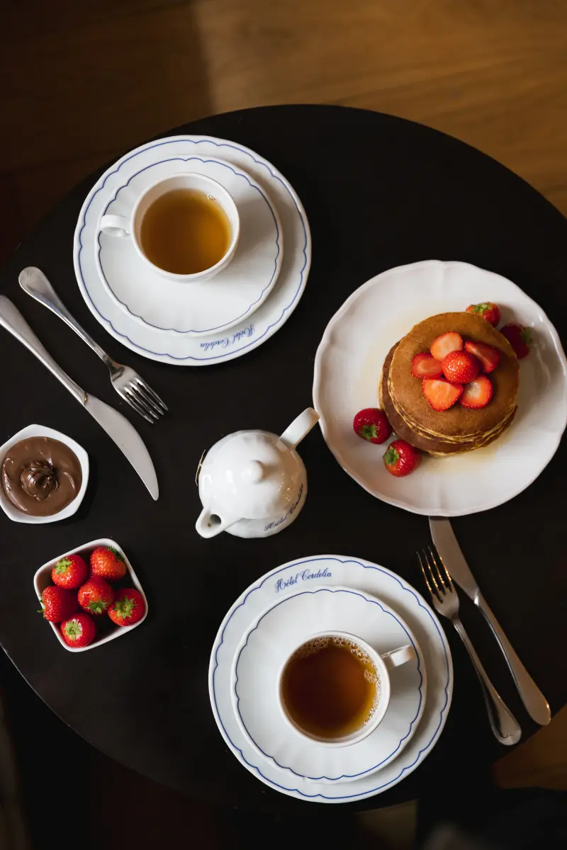 Table ronde noire avec service tea time pour deux : tasses Hotel Cordelia, pancakes aux fraises et theiere