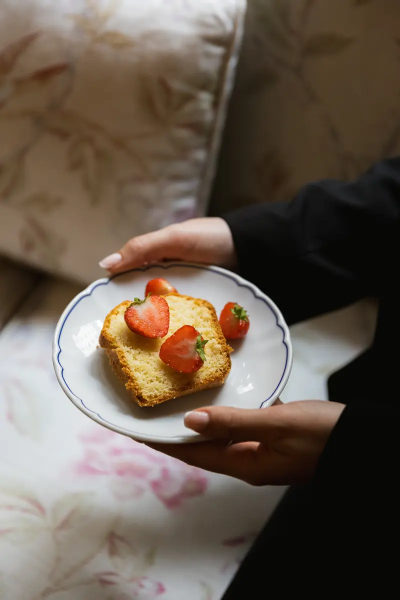 Mains tenant une assiette Hotel Cordelia avec une tranche de cake maison garni de fraises fraiches